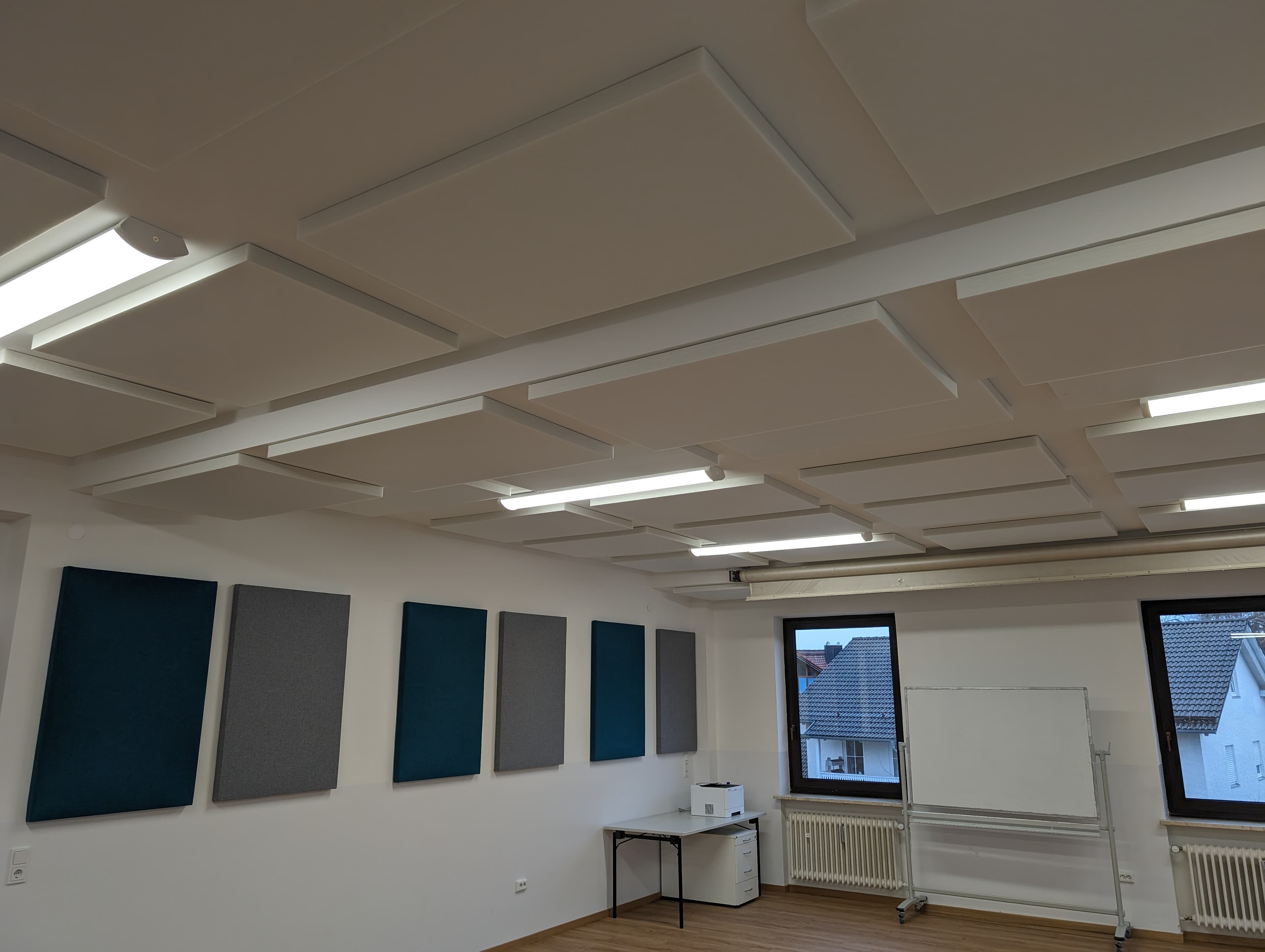 Schulungsraum mit weißen Decken-Schallschutzelementen und blau/grauen Wandpaneelen aus Merino-Stoff.